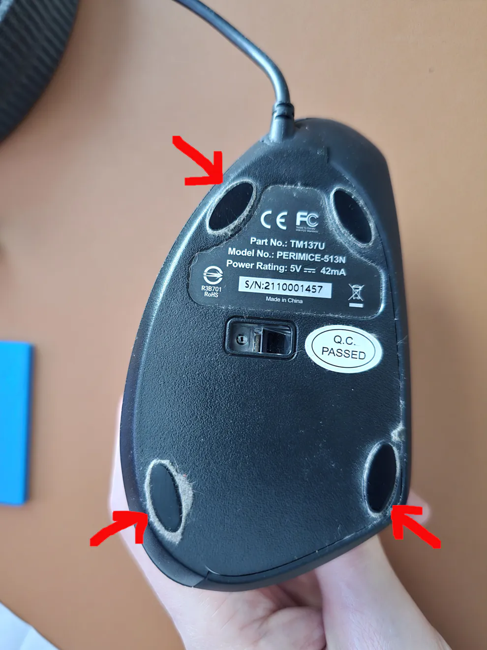 Bottom of computer mouse. Three arrows are drawn to the top left and bottom two computer feet.